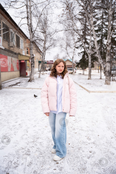 Скачать 15-летняя русская девушка в светло-голубых джинсах и зимней куртке стоит на фоне заснеженных берез на фоне города. Она излучает естественную красоту, элегантность и энергию молодости фотосток Ozero