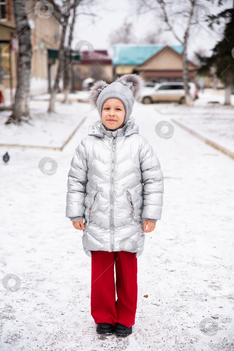 Скачать 8-летняя русская девочка улыбается на фоне снега, одетая в теплую зимнюю куртку и шапку. Она стоит на улице на фоне снежного пейзажа и смотрит в камеру с радостным, игривым выражением лица фотосток Ozero