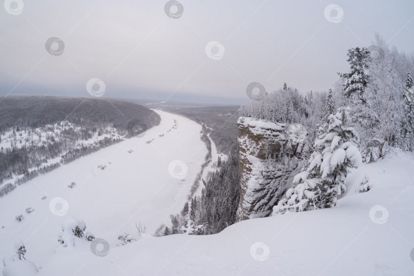 Скачать Скалистый, покрытый снегом утес над замерзшей рекой. фотосток Ozero