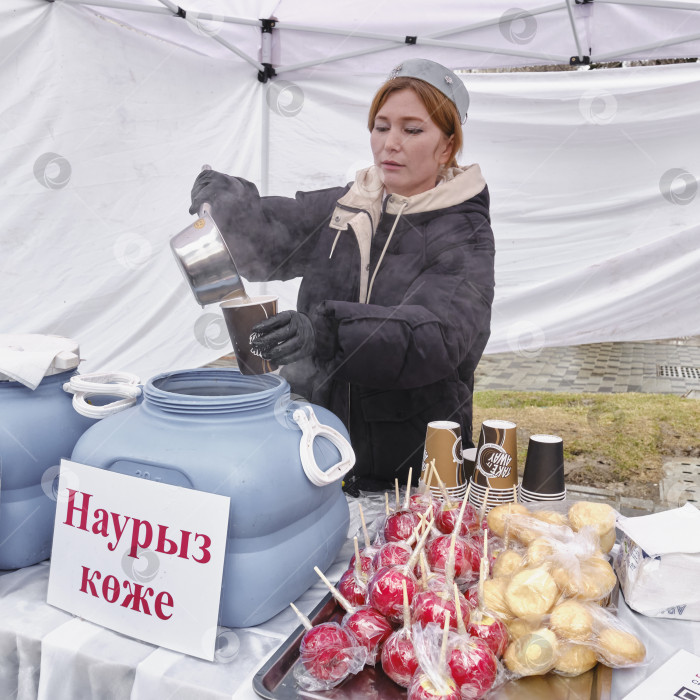 Скачать Женщина разливает национальный суп казахской кухни на праздник Наурыз в бумажный стаканчик у торговой палатки. фотосток Ozero