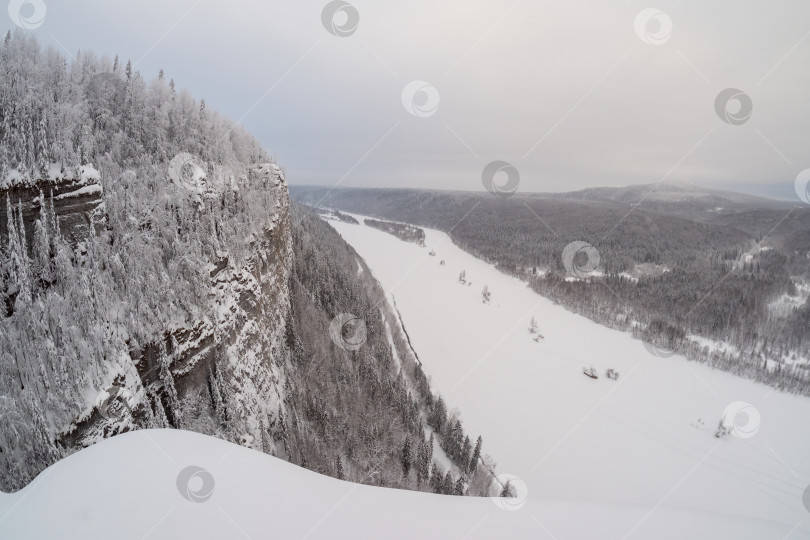 Скачать Скалистый, покрытый снегом утес над замерзшей рекой. фотосток Ozero