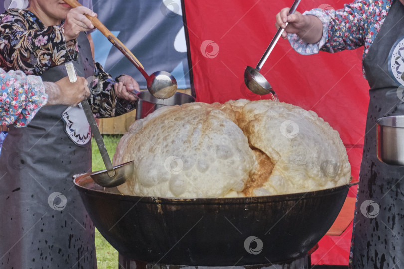 Скачать Женские руки половниками поливают маслом огромный баурсак, который жарится в чане фотосток Ozero