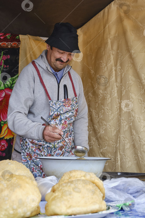 Скачать Кулинарный мастер-класс по приготовлению баурсаков, кусочков теста, обжариваемых во фритюре. Мужчина держит в руке половник фотосток Ozero