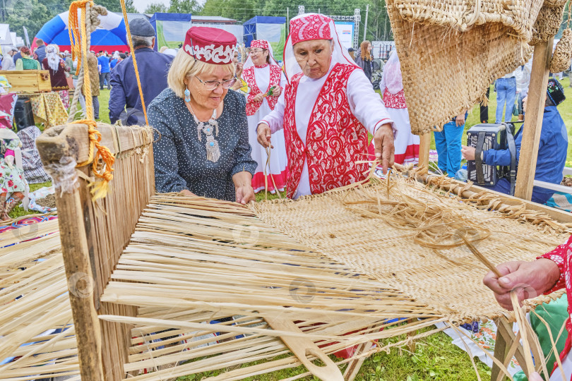 Скачать Пожилые азиатские женщины ткут лыко на деревянном ткацком станке на фестивале сибирских татар. фотосток Ozero