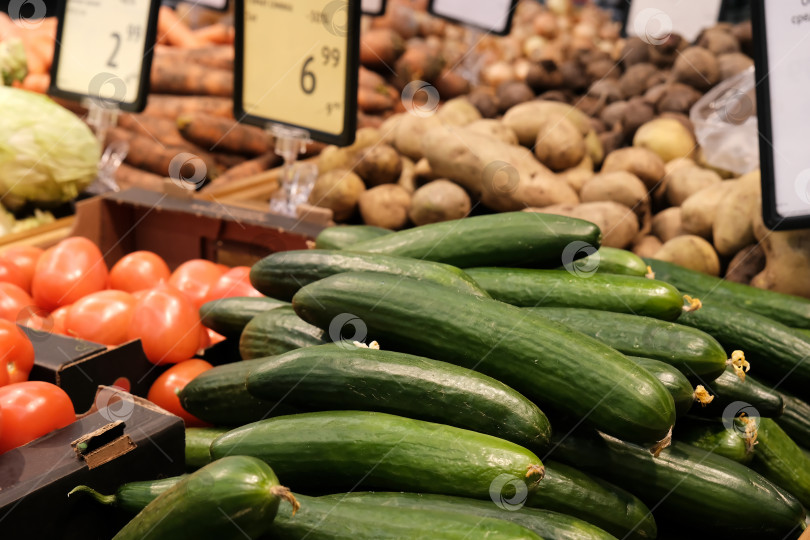 Скачать Овощи с продовольственного рынка с ценником. Различные свежие спелые огурцы, помидоры, картофель и другие сельскохозяйственные продукты, выставленные на продажу на рынке фотосток Ozero