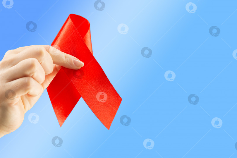 Скачать Концепция здравоохранения и медицины. Осведомленность о СПИДе. Женская рука держит красную ленту для информирования о СПИДе на синем фоне с местом для текста. Международный день борьбы со СПИДом фотосток Ozero