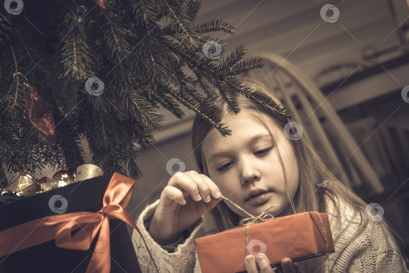 Скачать Счастливого Рождества, счастливых праздников. Веселая симпатичная маленькая блондинка открывает рождественский подарок фотосток Ozero