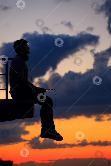 Скачать Мужчина слушает музыку на крыше. Облака и закат фотосток Ozero