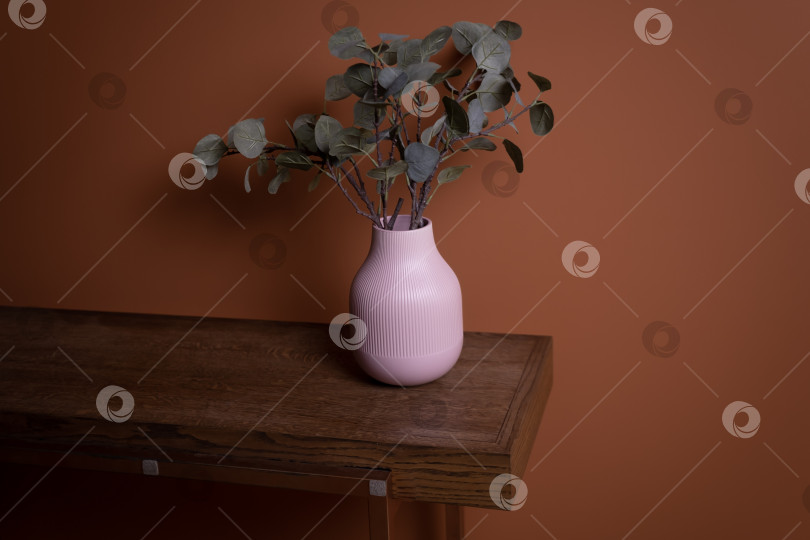 Скачать розовая ваза с зеленым растением стоит на коричневом деревянном столе на фоне оранжевой стены фотосток Ozero