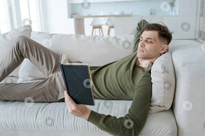Скачать Мужчина читает книгу на диване фотосток Ozero