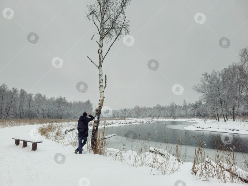 Скачать мужчина облокотился на березу, глядя на зимнюю реку фотосток Ozero