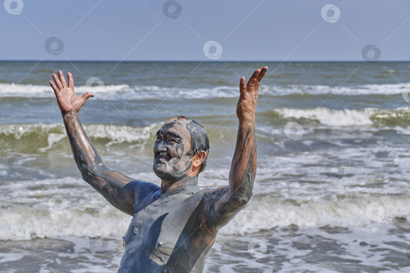 Скачать Пожилой мужчина, покрытый лечебной грязью на морском пляже, наслаждается жизнью фотосток Ozero