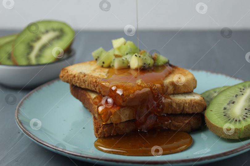 Скачать Полезный завтрак в отеле. Тосты с медом и кусочками фруктов и киви на сером фоне фотосток Ozero