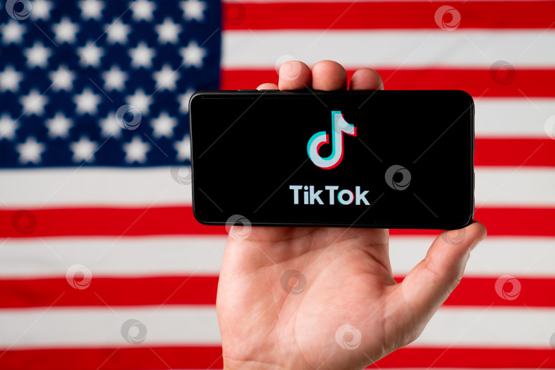 Скачать Логотип приложения Tiktok на смартфоне на фоне американского флага. Дональд Трамп намерен запретить Tiktok в США. Россия, Казань - 08 августа 2020 г. фотосток Ozero