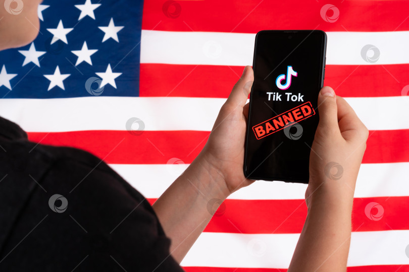 Скачать Подросток держит в руках смартфон с логотипом Tiktok на фоне американского флага. Избирательный подход. Дональд Трамп намерен запретить Tiktok в США. Россия, Казань - 08 августа 2020 г. фотосток Ozero