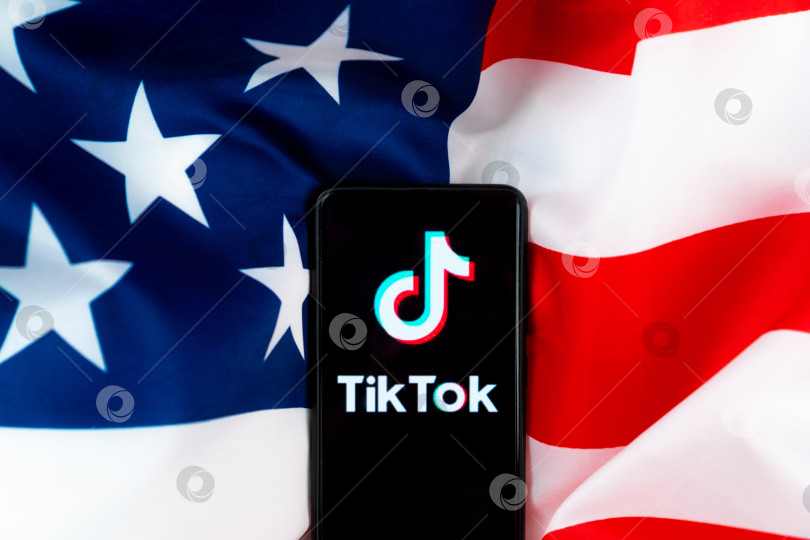 Скачать Логотип приложения Tiktok на смартфоне на фоне американского флага. Дональд Трамп намерен запретить Tiktok в США. Россия, Казань - 08 августа 2020 г. фотосток Ozero