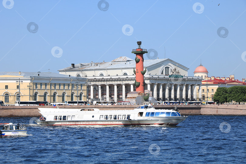 Скачать Россия, Петербург, 8 июня 2019 года. Стрелка Васильевского острова. На фото Ростральная колонна и здание Фондовой биржи на берегу Невы на фоне неба и прогулочный катер с туристами, любующимися видами города. фотосток Ozero