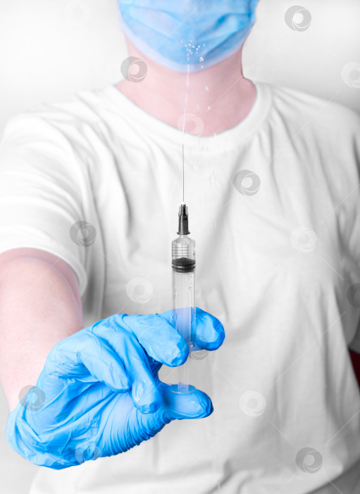 Скачать Шприц с каплями лекарства в руке медицинского работника в медицинских перчатках и маске. Сосредоточьтесь на переднем плане. фотосток Ozero