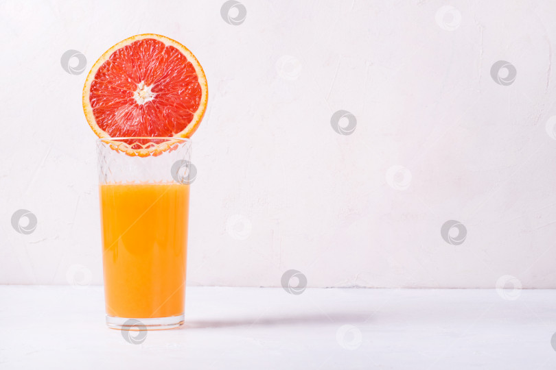 Скачать Свежевыжатый кроваво-апельсиновый сок в стакане для питья с половинкой фрукта сверху на белом фоне. фотосток Ozero