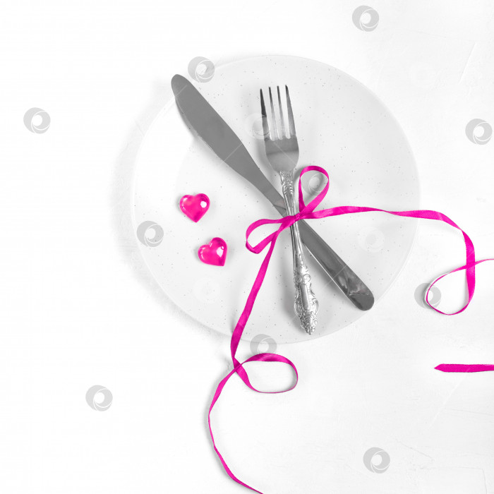 Скачать Вилка и нож украшены розовой лентой и декоративными сердечками на тарелке на белом фоне. фотосток Ozero