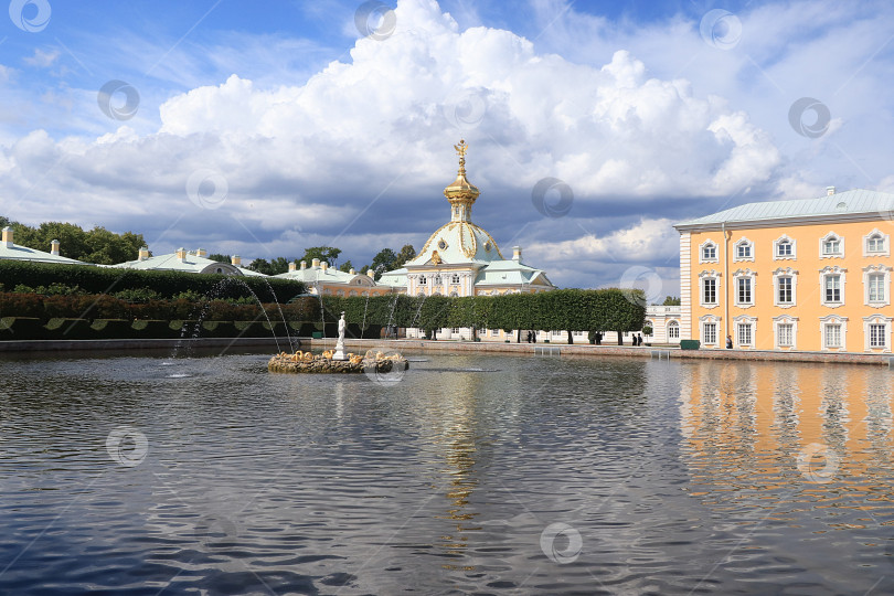 Скачать Россия, Санкт-Петербург, Петергоф, 8 июля 2019 года. На фото - главный придворный храм с двуглавым орлом на куполе в Верхнем парке Государственного музея-заповедника "Петергоф" и люди, которые прогуливаются по парку и любуются архитектурой. фотосток Ozero