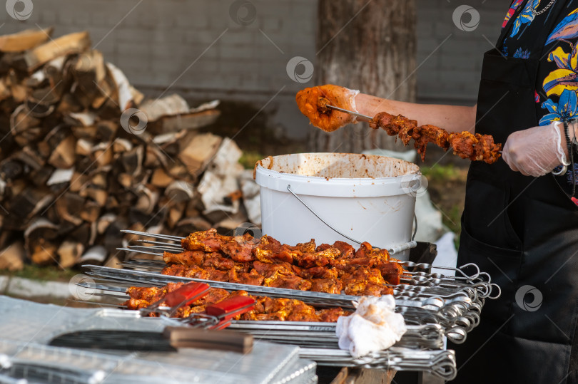 Скачать Повар нанизывает маринованное мясо на шампуры для жарки на гриле на заднем дворе на фоне кучи дров в камине. Общее представление о рецептах и технологии приготовления мясных блюд. фотосток Ozero