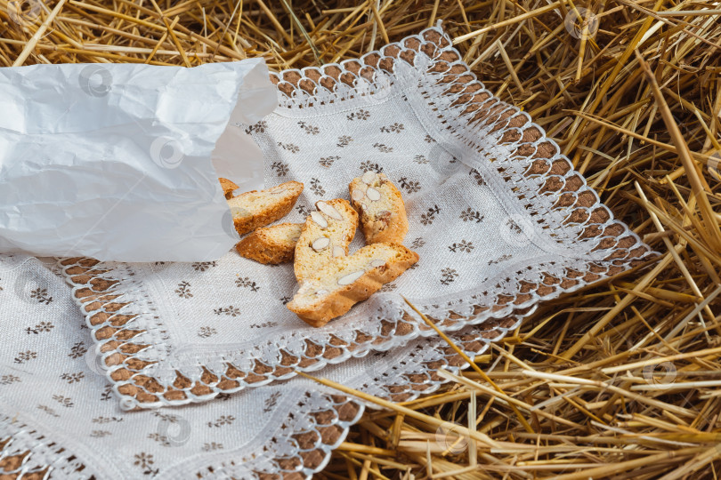 Скачать Миндальное печенье крекеры с кусочками орехов высыпались из бумажного пакета на салфетку, лежащую на соломе фотосток Ozero