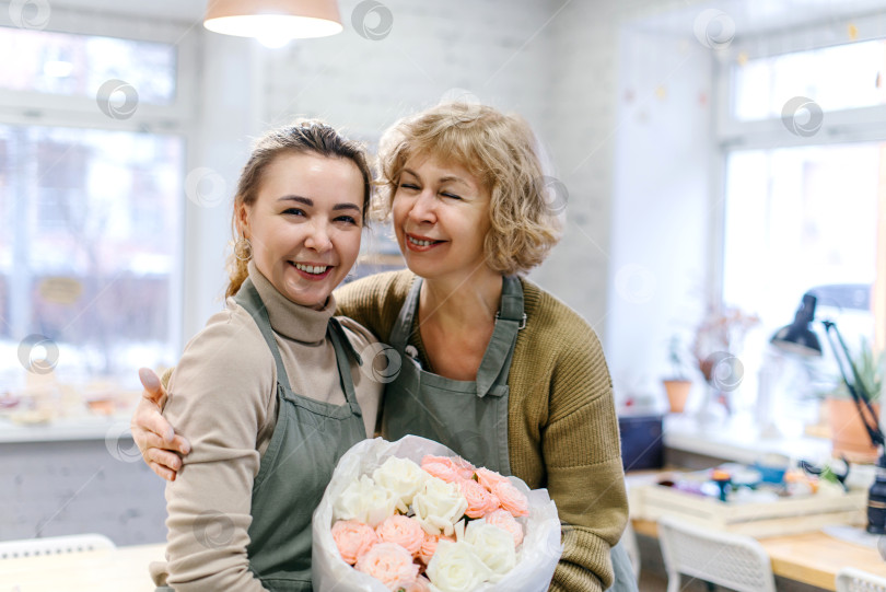 Скачать Мать и дочь обмениваются улыбками, держа в руках букет в цветочной мастерской фотосток Ozero