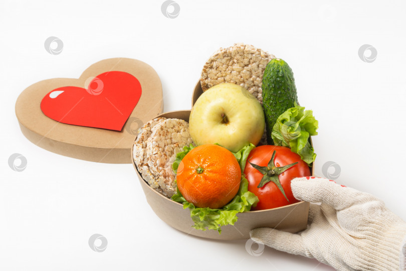 Скачать В руке человек держит коробку с полезными для здоровья овощами и фруктами. Коробка и крышка в форме сердца. Концепция здорового питания фотосток Ozero