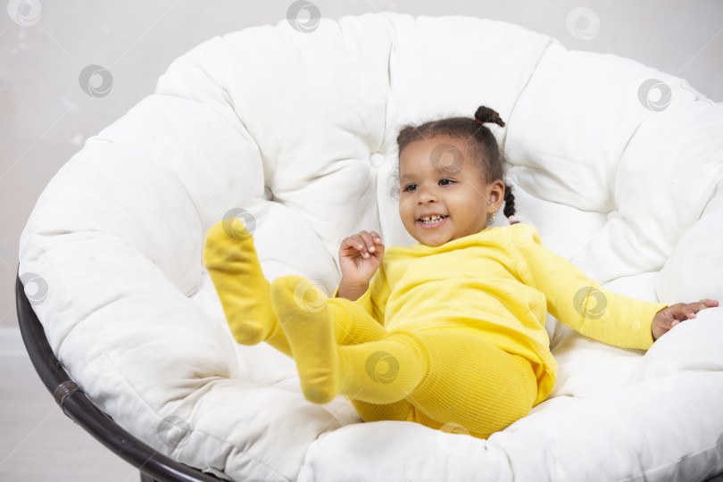 Скачать Маленькая афроамериканка балуется и играет в мягком кресле. фотосток Ozero