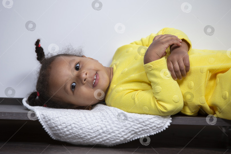 Скачать Маленькая афроамериканка в желтом платье лежит и улыбается. фотосток Ozero