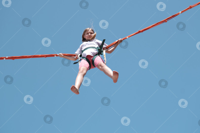 Скачать Маленькая девочка подпрыгивает высоко в воздухе на тарзанке-батуте фотосток Ozero