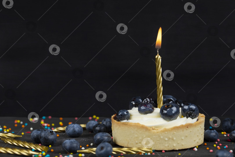 Скачать На темном фоне торт с горящей свечой, посыпанный черными ягодами. фотосток Ozero