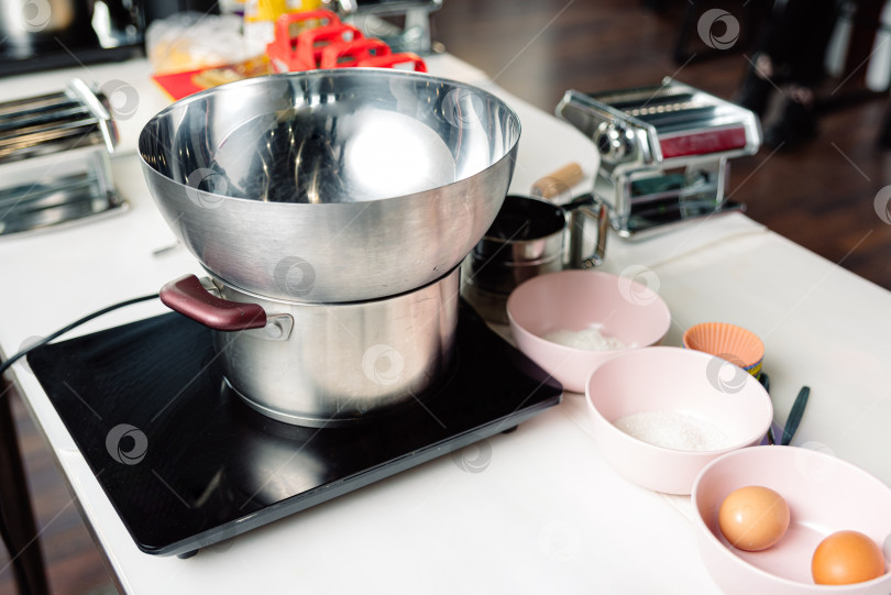 Скачать кухонные принадлежности на столе на кухне у себя дома. миска и сотейник из нержавеющей стали, электрическая плита, миски с ингредиентами фотосток Ozero