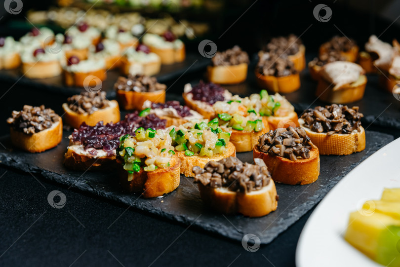Скачать концепция кейтеринга, еды и напитков - крупный план различных брускетт с нарезанными кубиками овощами и грибами на черной грифельной доске фотосток Ozero