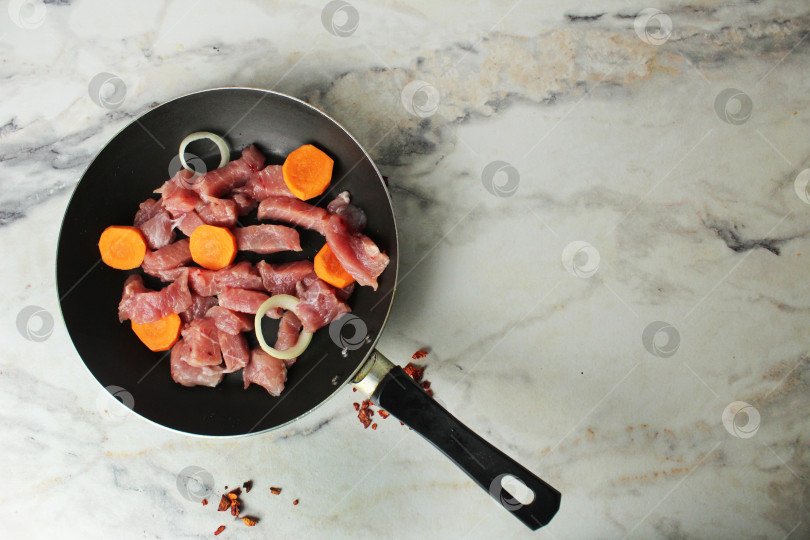 Скачать Кусочки сырого свиного мяса с овощами, луком, морковью на сковороде, вид сверху copyspace фотосток Ozero