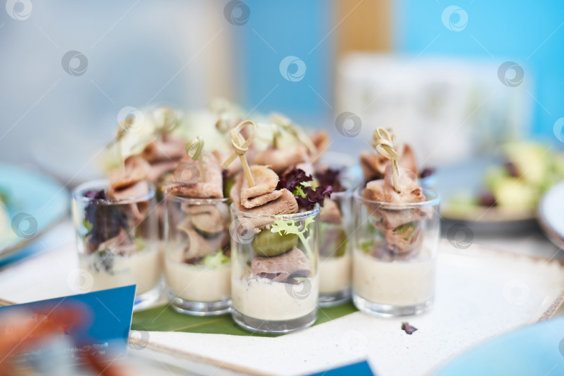 Скачать Вкусные закуски с оливками и мясом в стеклянных стаканчиках на банкетном столе для фуршета. Деликатесы крупным планом, закуска, антипасти фотосток Ozero