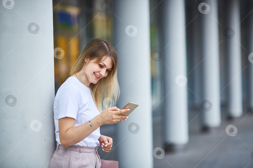 Скачать Молодая женщина улыбается, держит в руках смартфон и смотрит на него. фотосток Ozero