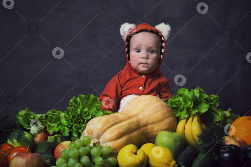 Скачать Маленький ребенок сидит рядом со свежими овощами и фруктами. фотосток Ozero