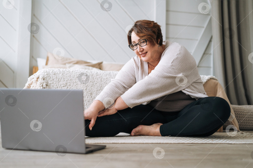 Скачать Взрослая очаровательная брюнетка плюс размер тела позитив практикует йогу с ноутбуком дома фотосток Ozero