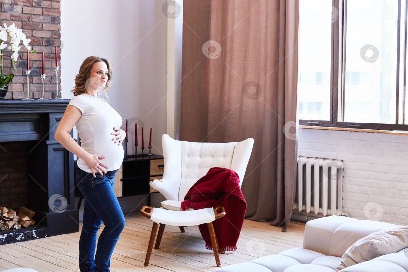 Скачать беременная девушка стоит в гостиной и трогает свой живот. фотосток Ozero