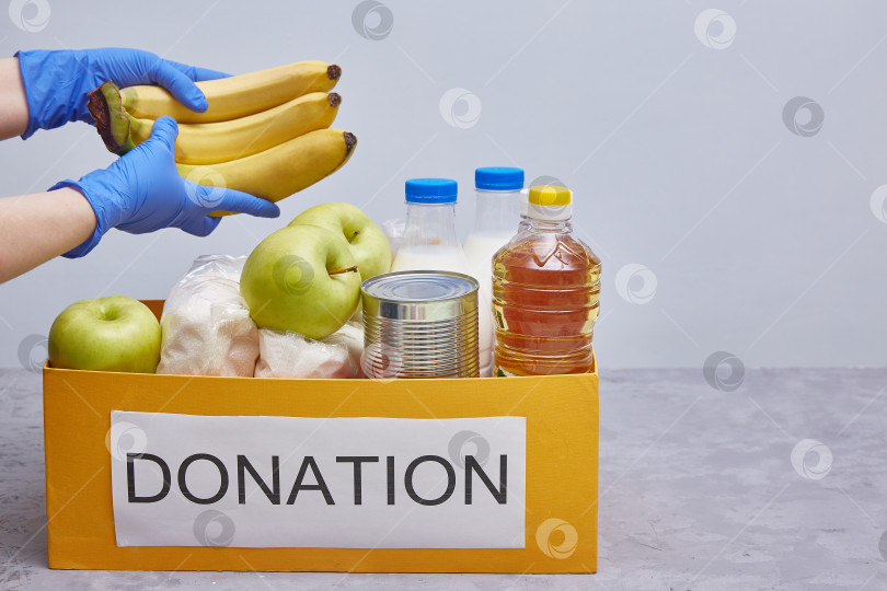 Скачать пожертвования и материальная помощь продуктами питания во время пандемии коронавируса. Руки в защитных синих перчатках берут или раскладывают еду. фотосток Ozero