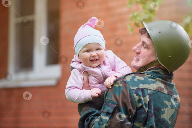 Скачать Военный в каске с улыбающимся маленьким ребенком на руках фотосток Ozero