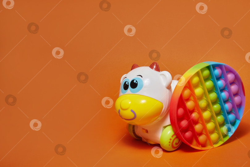 Скачать антистрессовая игрушка pop it и игрушечная корова на оранжевом фоне с пространством для копирования фотосток Ozero