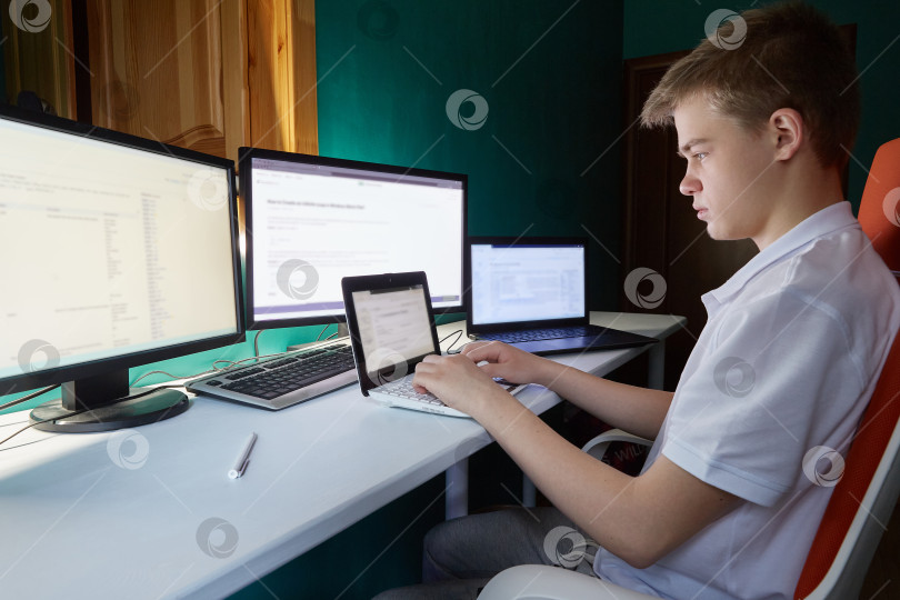 Скачать Парень-подросток сидит и смотрит за множество мониторов. фотосток Ozero