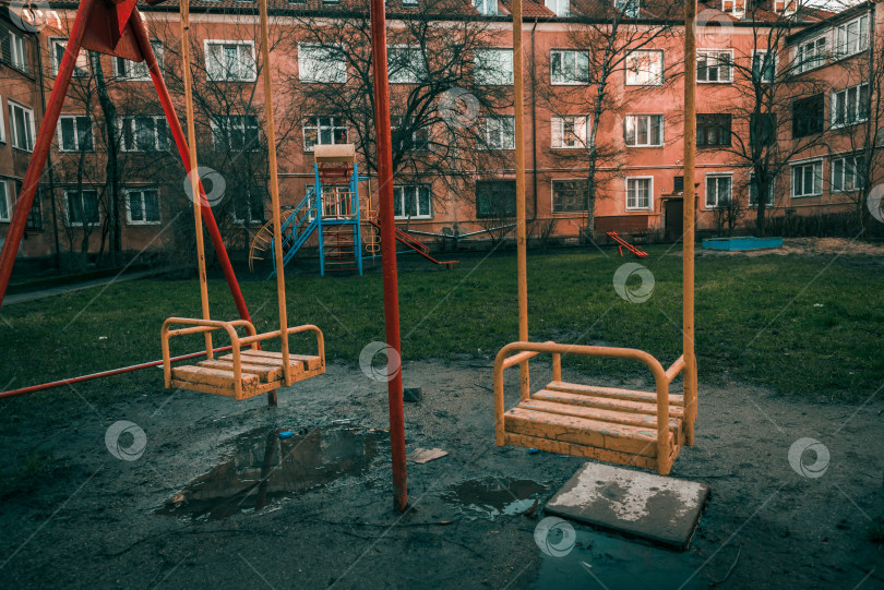 Скачать Дети качаются на качелях в пустом дворе многоэтажного дома, пасмурный осенний день фотосток Ozero