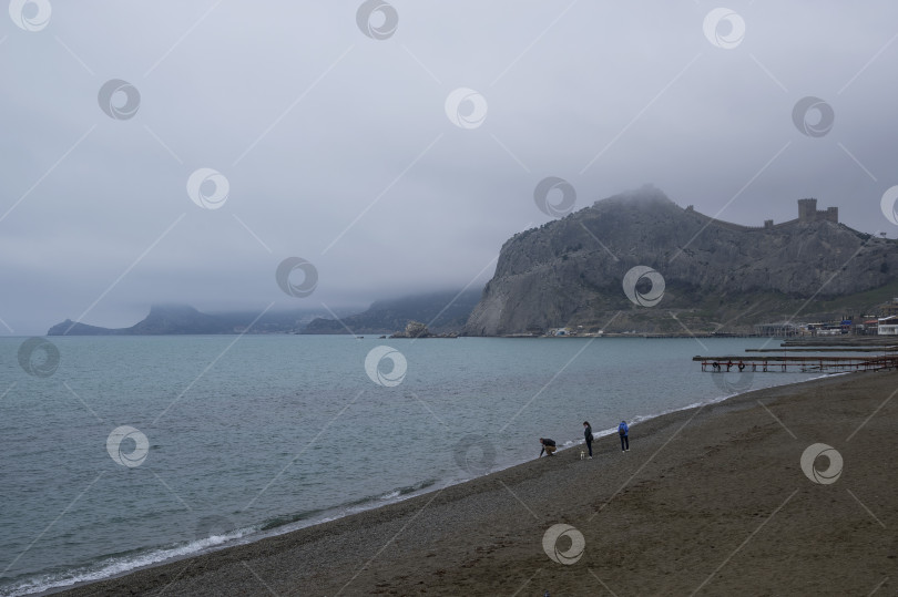 Скачать Три человека прогуливаются по пустому пляжу - межсезонье. фотосток Ozero