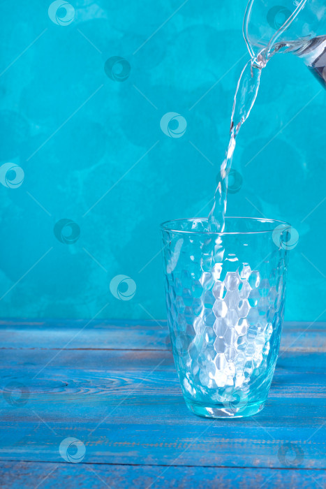 Скачать Очищенная вода наливается в стакан для питья из кувшина на бирюзовом фоне. фотосток Ozero