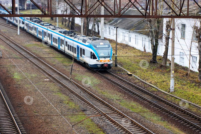 Скачать Беларусь, Минск - 02.01.2025: Впереди по железнодорожным путям движется бело-голубой поезд фотосток Ozero