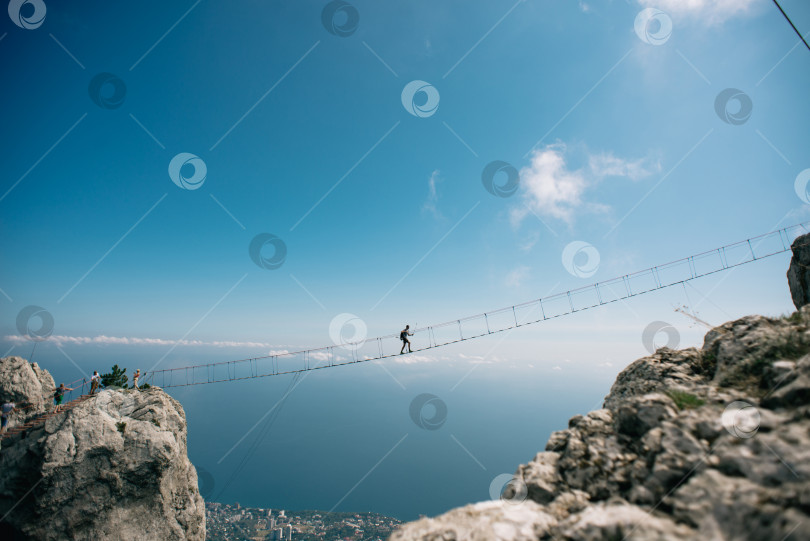 Скачать Мужчина идет по подвесному мосту между крымскими горами Ай-Петри. фотосток Ozero